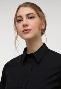 Black, button-down shirt with a collared neckline. Smooth fabric, fitted design, and visible stitching details along the collar and placket.