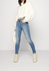 Vit, texturerad stickad croppad tröja med överdimensionerade ärmar. Ljusblå, slitna skinny jeans. Beiga plattformssneakers. Minimalistisk vit handväska.