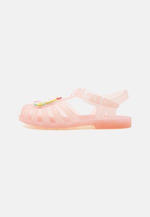 Sandale en gelée transparente rose pailletée avec une bride de boucle à la cheville et une décoration arc-en-ciel colorée sur les orteils.