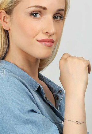 Silver bracelet with intertwined links and a central red accent. Model wears a denim shirt, displaying the bracelet on her wrist.