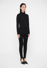 Mustast lõngast kõrge kraega kampsun, mida kantakse koos keha järgsete mustade pükstega. Modell kannab teravate ninaosadega musti kingi. Tekstuuriga kangas üle kogu pinna.