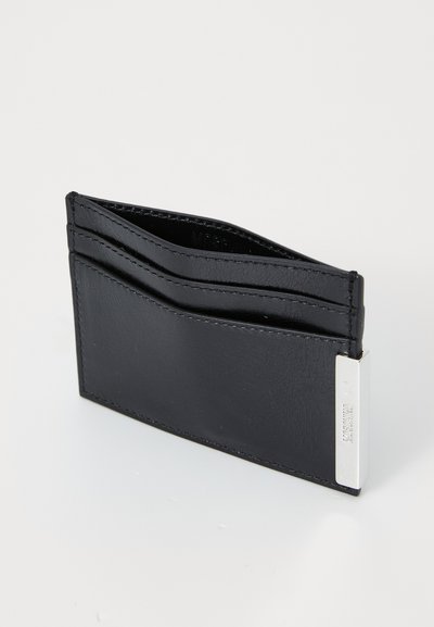 Svart läder kortfodral med flera fack, slät yta och en silverfärgad metallaccent på ena sidan. Har en minimalistisk design.