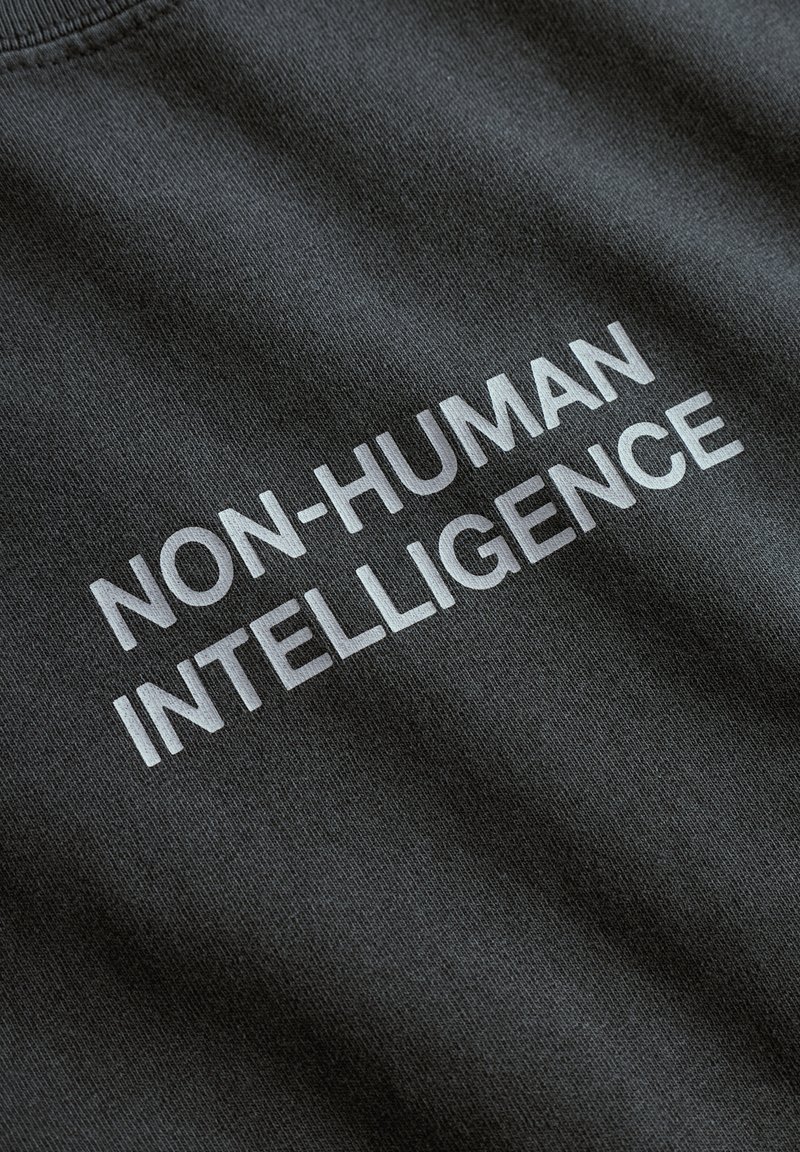 Un tissu noir au toucher lisse présente la phrase "INTELLIGENCE NON-HUMAINE" en lettres blanches en gras.