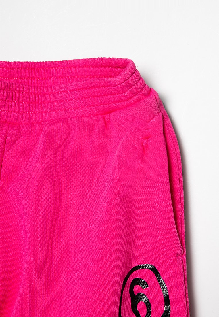 Fuchsia Jogginghosen mit elastischem Bund, strukturiertem Stoff, Seitentaschen und einem schwarzen runden Logo-Detail am unteren Bein.
