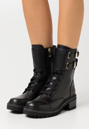 Bottes chelsea en cuir noir avec un design à lacets, fermeture éclair à l'avant et boucles dorées. Semelle en caoutchouc texturée et épaisse pour une meilleure adhérence.