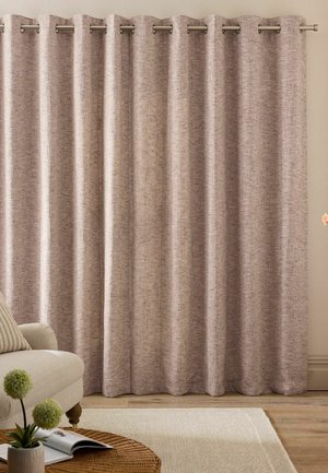 Tende marrone chiaro con trama appese su anelli metallici in un soggiorno con divano beige, tavolo in vimini, piante e tappeto chiaro su pavimento in legno.