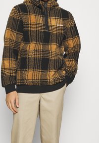 Pull-over en polaire avec un motif à carreaux noir et moutarde, doté d'un col demi-zip et de poignets et ourlet côtelés noirs.