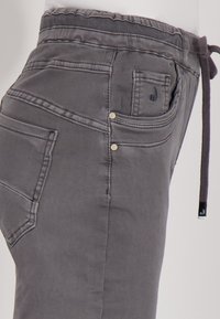 Grijze casual broek met een koord in de taille, zichtbare voor- en achterzakken, contrasterende stiksels en kleine klinknageldetails op de randen van de zakken.