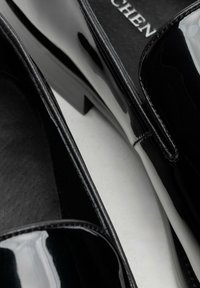 Czarne lakierowane buty ze skórą z połyskiem i niskim słupkowym obcasem, charakteryzujące się prostym, otwartym fasonem i przeszyciami wzdłuż krawędzi.