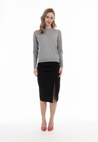 Pulover gri cu embellishments din bijuterii, asortat cu o fustă tip creion neagră cu o deschidere pe lateral. Modelul poartă tocuri roșii.