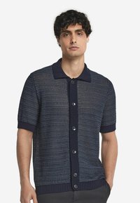 Marineblauwe kortekraag cardigan met een gestructureerd breiselontwerp, voorzien van een geribde kraag en knopen, geaccentueerd met lichte horizontale strepen.