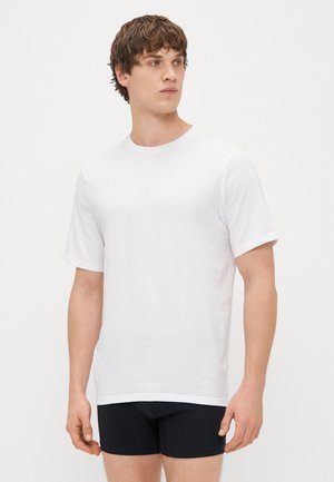 T-shirt en coton blanc avec un col rond et des manches courtes, présentant une coupe standard et une texture lisse, associé à un short noir.