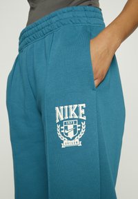 Teal Nike sweatpants med elastiskt midjeband och sidofickor. Har en vit logotyp och texten "Nike 1972 Oregon" med lagerbladaccent. 