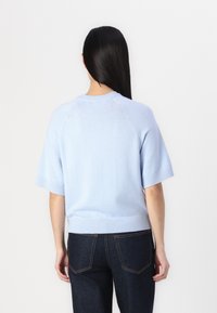 Hellblauer Strickpullover mit kurzen Ärmeln, geripptem Saum und Rückennaht-Details. Kombiniert mit dunkler Jeans.