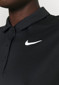 Svart polo skjorta i texturerad tyg med knapplist med tre knappar och en vit Nike swoosh-logotyp på vänster sida.