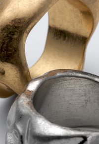 Κοντινό πλάνο δύο μεταλλικών δαχτυλιδιών, ενός χρυσού και ενός ασημένιου, που εμφανίζουν φθαρμένες και θαμπές επιφάνειες με στρογγυλεμένες και ακανόνιστες άκρες.