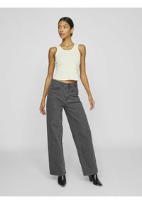 Světle šedý crop top, tmavě šedé široké kalhoty s vysokým pasem a černé kotníkové boty. Hladká textura, neformální design a přiléhavý silueta.