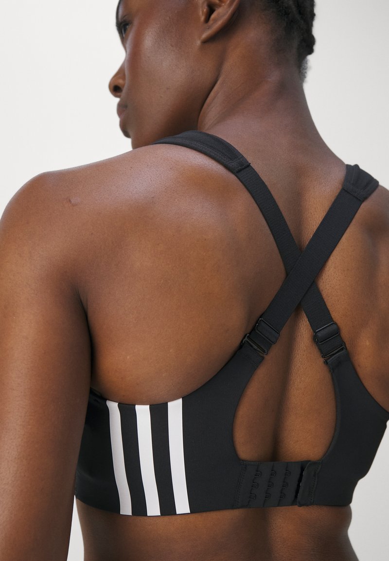 Top sportivo nero con design a schiena scoperta, spalline regolabili e tre strisce verticali bianche sul retro. Tessuto liscio ed elastico.