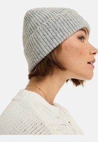 Lichtgrijze geribbelde gebreide beanie, met een zachte textuur en een strakke pasvorm. De muts heeft een opgerolde rand voor extra warmte en stijl.