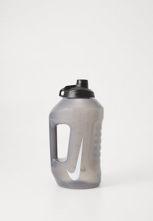 Nike water bottle in translucent gray plastic, featuring a black screw top lid, side handle, and white swoosh logo. Ergonomic design.