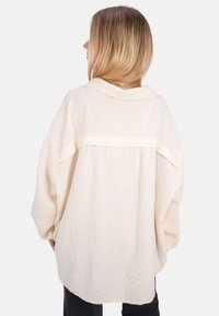 Cremfarbendes, übergroßes Hemd aus strukturiertem Baumwollstoff mit lockerer Passform, das über einen umgeschlagenen Kragen und eine Nahtdetails auf der Rückseite verfügt.