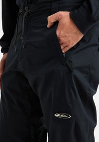 Tumši jūras flotes krāsas cargo bikses ar strukturētu apdari, ar regulējamu jostasvietu, sānu kabatām un logo uzlīmi uz augšstilba.