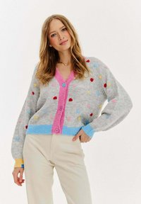 Szary kardigan z wielokolorowymi kropkami, różowym zapięciem na guziki z przodu oraz ryflowanymi niebieskimi i żółtymi mankietami. Miękka faktura i luźny krój.