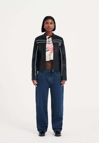 Svart läderjacka med vit kantning, kort design, i kombination med högmidjade blå denimjeans och svarta skor.