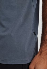 Grå kortærmet t-shirt lavet af blødt stof, med en glat tekstur, en sømdesign og en lille mærketiket på siden.