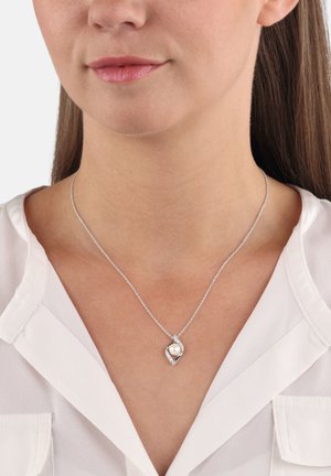 Donna che indossa una collana d'argento con un pendente a forma di diamante che presenta una perla centrale e piccole pietre circostanti.