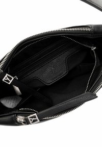 Wnętrze czarnej skórzanej torebki z zamykanymi na zamek przegródkami i miękką podszewką. Zawiera teksturowaną kieszeń z logo oraz srebrne elementy ozdobne.