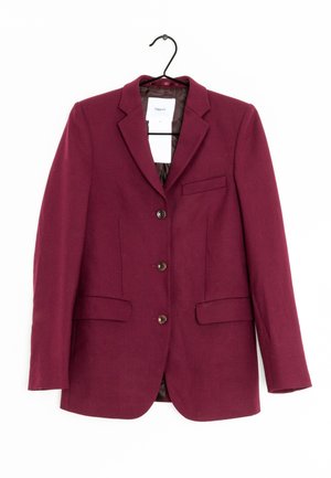 Blazer bordeaux cintré avec trois boutons, deux poches avant avec rabats et une poche poitrine passepoilée, suspendu sur un cintre noir sur fond blanc.