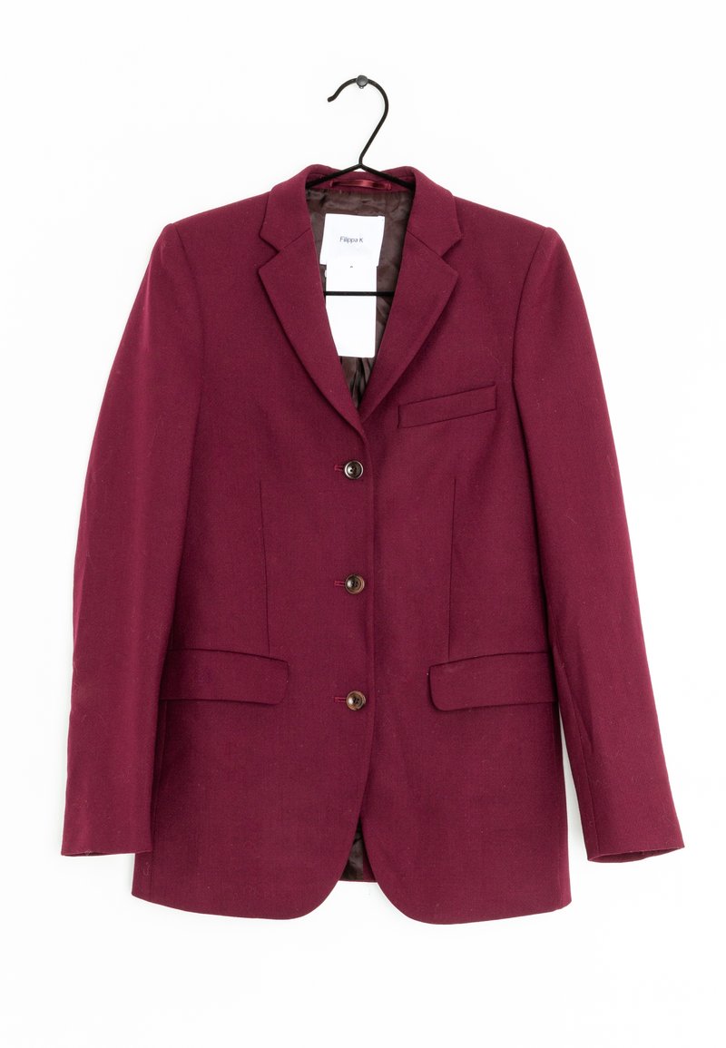 Blazer bordeaux cintré avec trois boutons, deux poches avant avec rabats et une poche poitrine passepoilée, suspendu sur un cintre noir sur fond blanc.