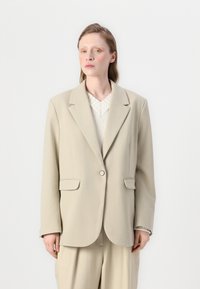 Béžový oversized blejzer s klopovým golierom, jedným gombíkovým zapínaním a dvoma prednými vreckami. Hladká tkanina so štruktúrovaným tvarom. Jemné široké detaily.