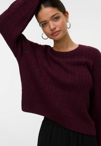 Maglione in cable-knit bordeaux con scollo rotondo e maniche ampie, caratterizzato da orlo a costine e dettagli texture su uno sfondo chiaro.