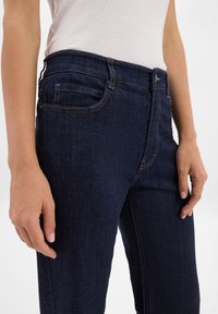 Ciemnoniebieskie dżinsy o slim fit, z wieloma kieszeniami i pomarańczowymi przeszyciami wzdłuż krawędzi i szwów.