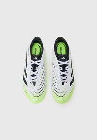 Zapatillas deportivas en blanco y negro con una parte superior texturizada, acentos verdes en la suela y cordones negros. Diseño aerodinámico para un mejor rendimiento.