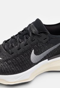Scarpa sportiva nera con tomaia in mesh testurizzato, dotata di un distintivo logo Nike bianco, lacci neri piatti e una suola bianca a contrasto.