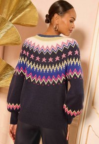 Granatowy sweter z wzorzystą karczką z różowymi, żółtymi i niebieskimi motywami zygzaków oraz gwiazd. Miękka tekstura, bufiaste rękawy i ribbowane wykończenie.