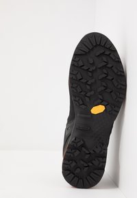 Czarna zewnętrzna podeszwa buta z wyraźnym, teksturowanym wzorem, z logo Vibram w kolorze żółtym. Zauważalne, wyraźne wzory bieżnika, zapewniające przyczepność.