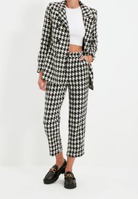 Completo di blazer e pantaloni in bianco e nero a motivo houndstooth con una vestibilità sartoriale. Il blazer ha un solo bottone. Mocassini neri piatti con accenti dorati.