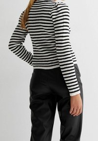 Pull côtelé rayé noir et blanc à manches longues, col arrondi et coupe ajustée, associé à un pantalon en simili cuir noir.