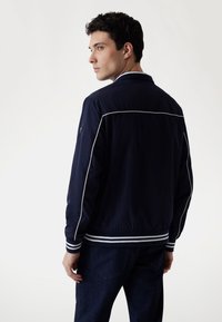 Navy bomberjack met witte accenten, geribbelde manchetten en een gestroomlijnd ontwerp. Bevat een stevige stof met een gladde textuur.