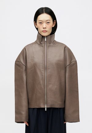 Bruine leren jas met hoge kraag, oversized pasvorm, ritssluiting aan de voorkant en brede mouwen. De textuur is glad met een matte afwerking.