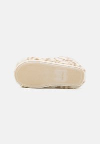 Fuzzy slipper sole in beige with a textured grip pattern. Soft fabric at the top in a similar color, providing a cozy appearance.