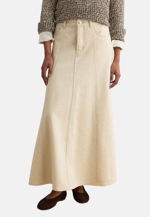 Woman wearing a beige A-line denim skirt with front seam details, paired with a brown textured sweater and dark brown flat shoes.