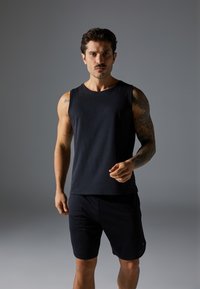 Black sleeveless athletic tank top in a soft fabric, paired with dark shorts, showcasing a fitted design and comfortable style.
