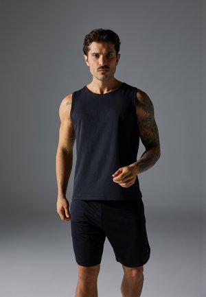 Schwarzes ärmelloses Sporttanktop aus weichem Material, kombiniert mit dunklen Shorts, das eine figurbetonte Passform und einen bequemen Stil zeigt.