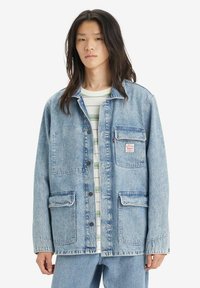 Svetlo modra jeans jakna s ovratnikom in tremi sprednjimi žepi. Ima gumbno zapiranje in majhen oznak na prsih.