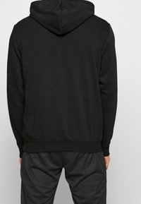 Felpa nera con cappuccio, dal tessuto liscio e orlo a coste, progettata per il comfort, abbinata a pantaloni scuri. Design semplice e funzionale.